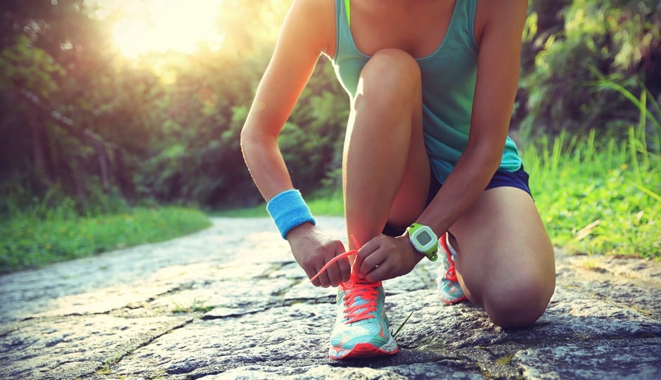 young woman runner tying shoelaces on stone trail