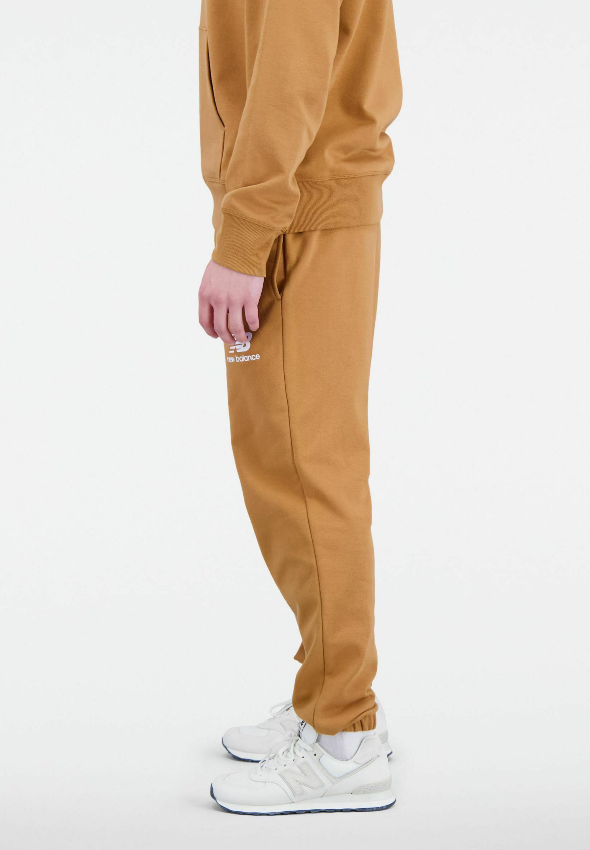 Pantalones jogger de algodón marrón con cintura ajustable, bolsillos laterales y detalle de logo en blanco. Combinados con zapatillas blancas con acentos grises.