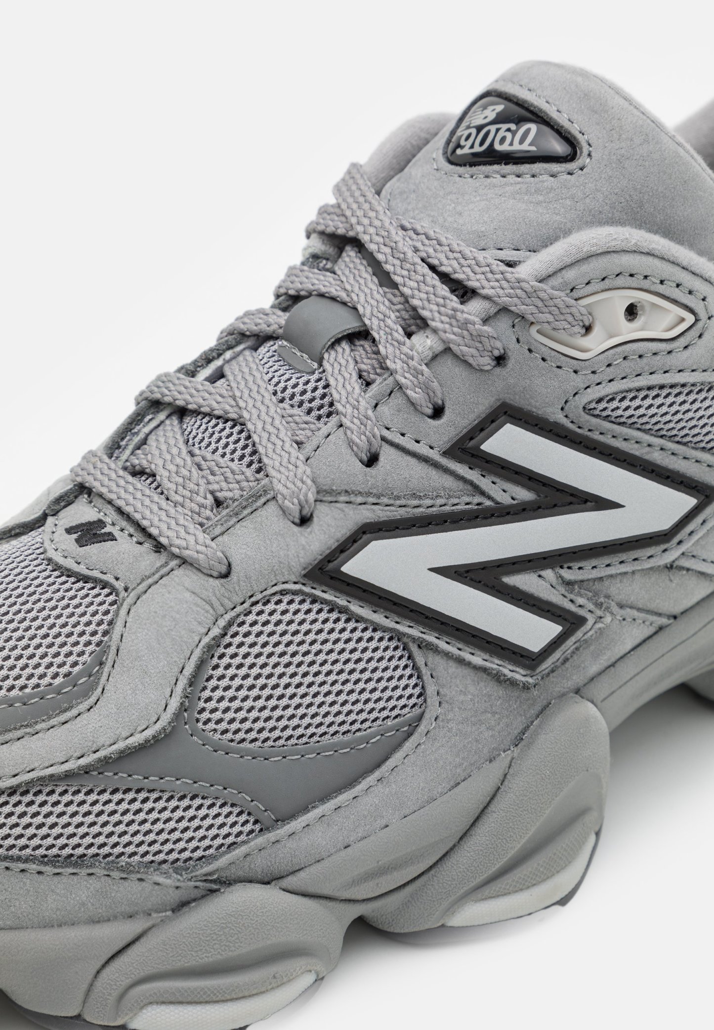 Primer plano de una zapatilla New Balance 9060 gris con paneles de malla, suela gruesa texturizada y cordones cruzados.