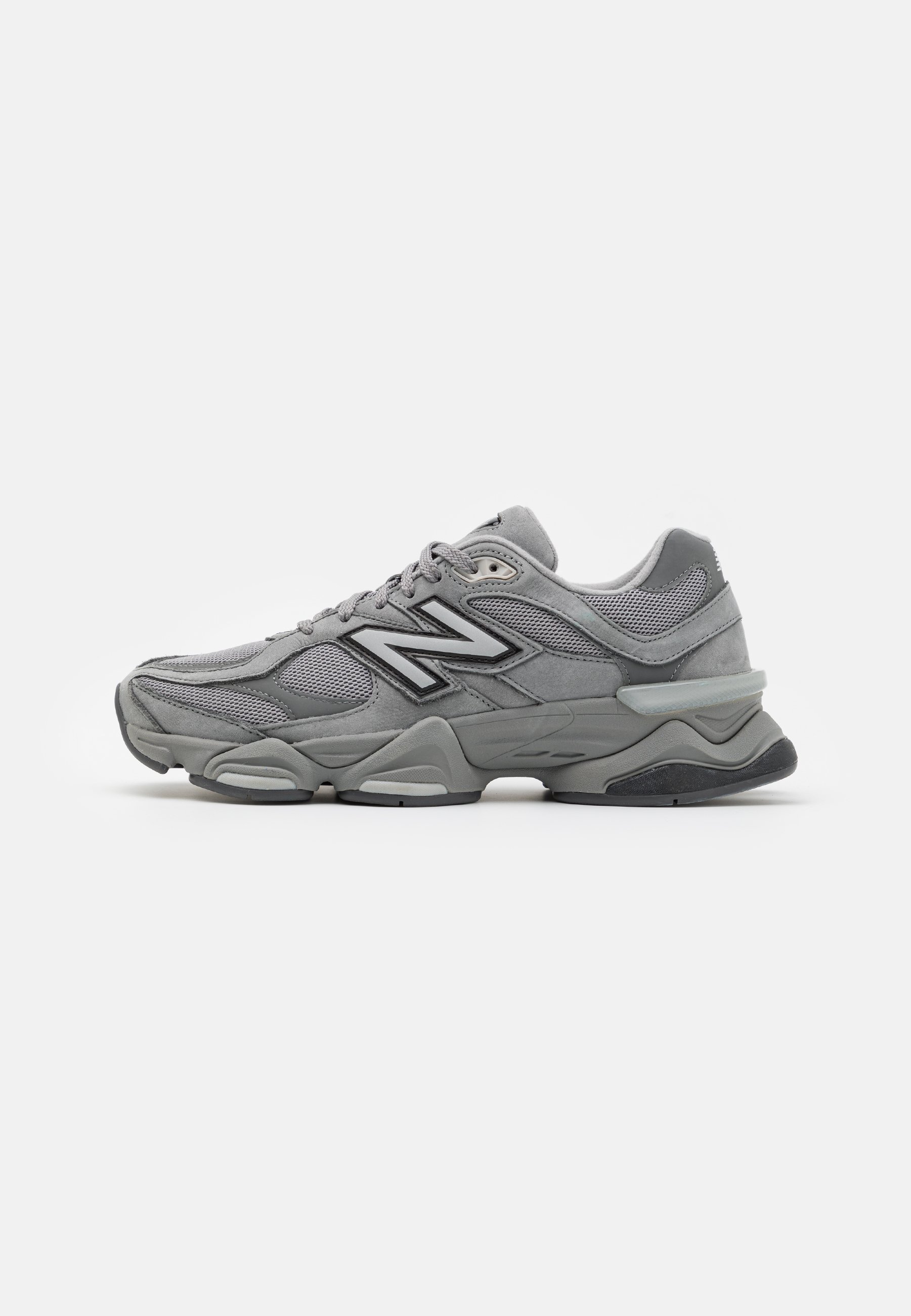 Zapatilla deportiva gris con paneles de malla y ante, suela gruesa acolchonada, cordones y un gran logo "N" en el lateral.