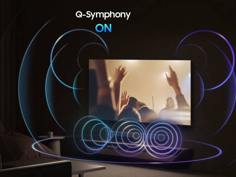 Le texte indique « Q-Symphony ON ». Appareil audio sans fil avec haut-parleurs circulaires concentriques bleus brillants et écran affichant une image aux tons chauds. Fond sombre avec visualisation sonore éclairée.