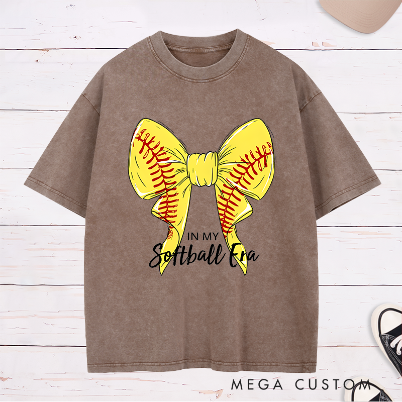 Personalized Softball Era Washed T-Shirt Design Showcasing a Vibrant Yellow Bow Inspired by Softball Stitching Paired with Customizable Text Perfect for Teams Players and Fans to Celebrate Their Love for the Game in Style