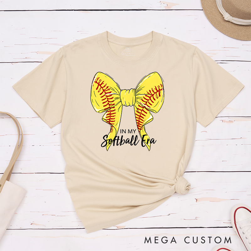 Personalized Softball Era T-Shirt Design Showcasing a Vibrant Yellow Bow Inspired by Softball Stitching Paired with Customizable Text Perfect for Teams Players and Fans to Celebrate Their Love for the Game in Style