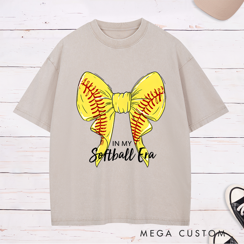 Personalized Softball Era Washed T-Shirt Design Showcasing a Vibrant Yellow Bow Inspired by Softball Stitching Paired with Customizable Text Perfect for Teams Players and Fans to Celebrate Their Love for the Game in Style