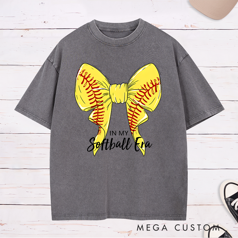Personalized Softball Era Washed T-Shirt Design Showcasing a Vibrant Yellow Bow Inspired by Softball Stitching Paired with Customizable Text Perfect for Teams Players and Fans to Celebrate Their Love for the Game in Style