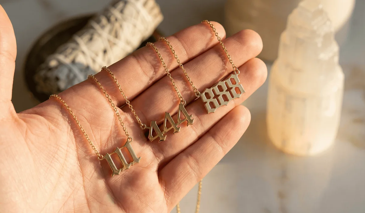 A selection of gold angel number necklaces (111, 444, 888) being held in a hand, symbolizing divine alignment and spiritual jewelry.