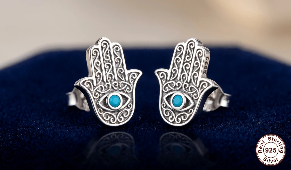 Detailed sterling silver Hamsa hand stud earrings with blue evil eye stone center on navy blue velvet.