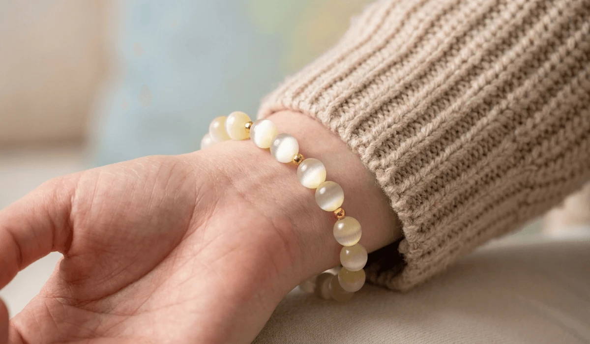 Close-up of a natural Satin Spar gemstone bead bracelet worn on a wrist showing silky cat-eye light reflection.