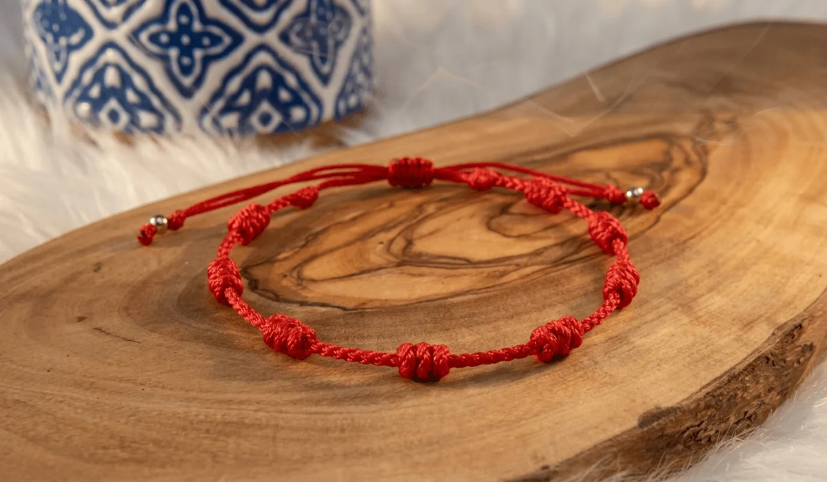 Macro shot of an authentic red string protection bracelet with traditional sacred knots on a rustic dark wood surface.