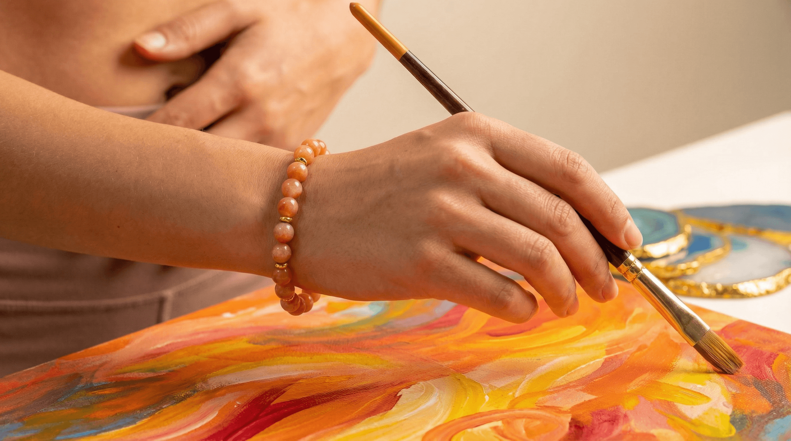 A person wearing a sacral chakra bracelet while painting, symbolizing the connection between healing stones and artistic inspiration.