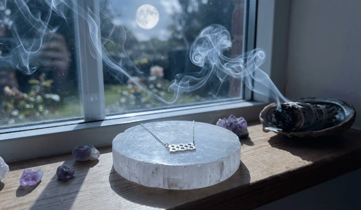 An angel number necklace being cleansed and charged on a selenite plate under the light of a full moon.