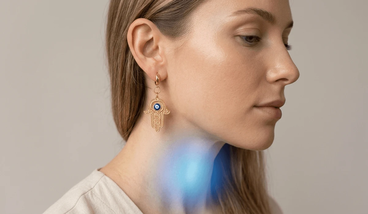 Woman wearing gold Hamsa hand drop earrings illustrating throat chakra energy alignment and divine protection.