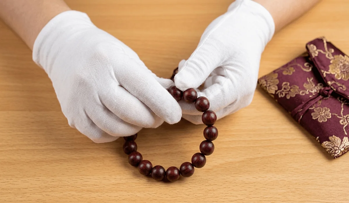 Hands wearing white cotton gloves polishing red sandalwood beads to create a natural wood patina.