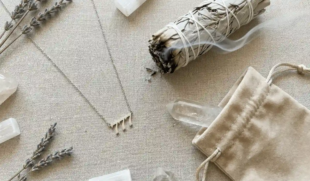 A spiritual jewelry cleansing ritual featuring an angel number necklace, sage smudge stick, and quartz crystal.