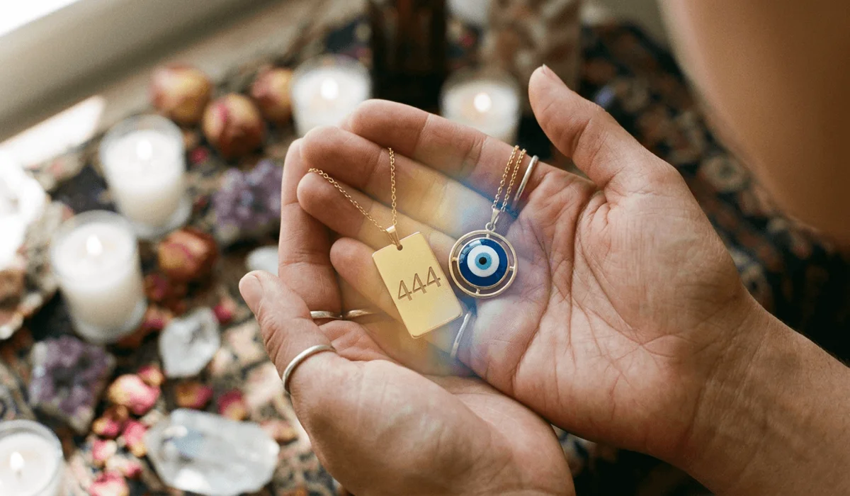A close-up of hands activating a 444 necklace and Evil Eye charm with a glowing blue and gold spiritual energy aura.