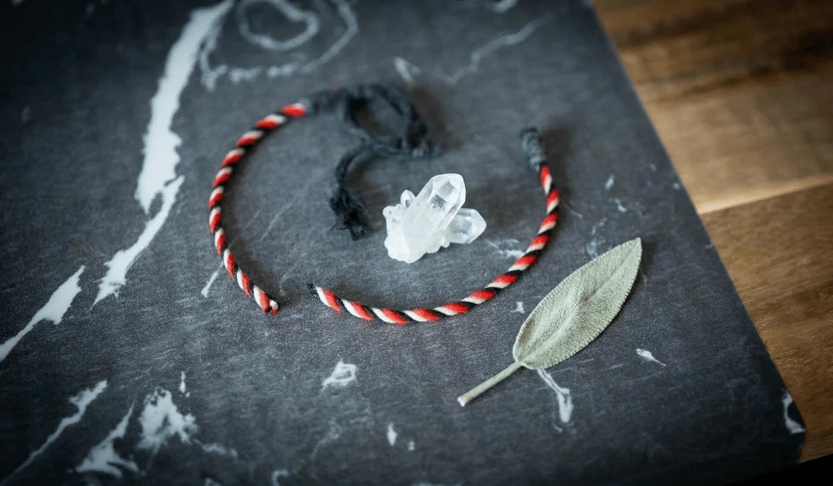 A broken red string bracelet on a wooden table with a crystal, symbolizing the release of negative energy and a completed spiritual mission.