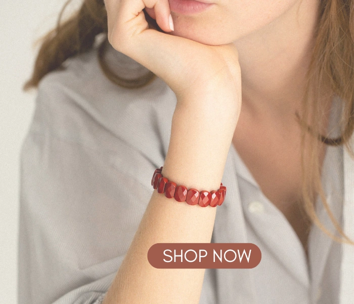 Close-up of a woman in a gray shirt wearing a Red Jasper Flat Beaded Bracelet, with a "SHOP NOW" button overlay.