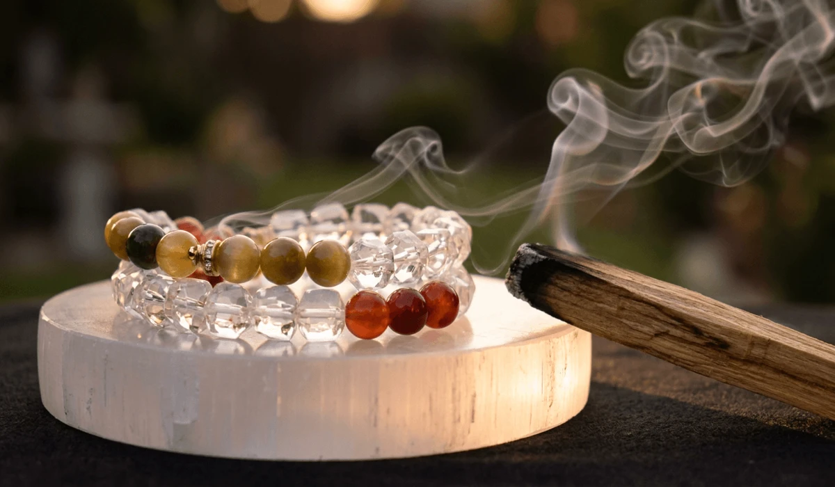 Gemstone mala beads resting on a selenite charging plate with cleansing palo santo smoke