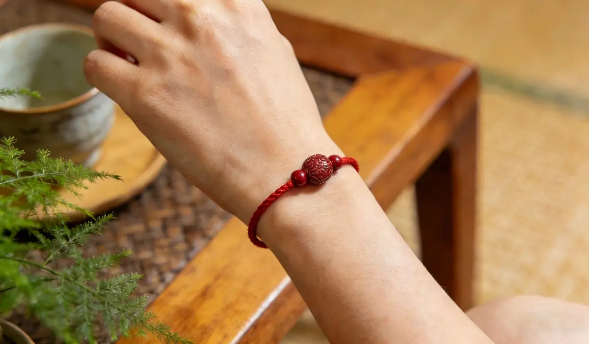 A cinnabar bead bracelet on red string worn on the wrist, representing daily protection, grounding energy, and root chakra balance in Feng Shui.