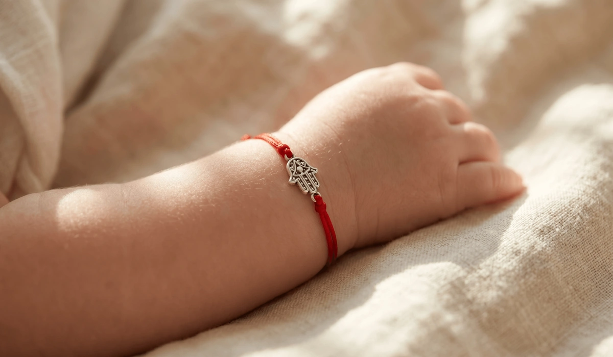 A newborn baby wearing a red string protection bracelet with a silver Hamsa charm for spiritual grounding and safety.