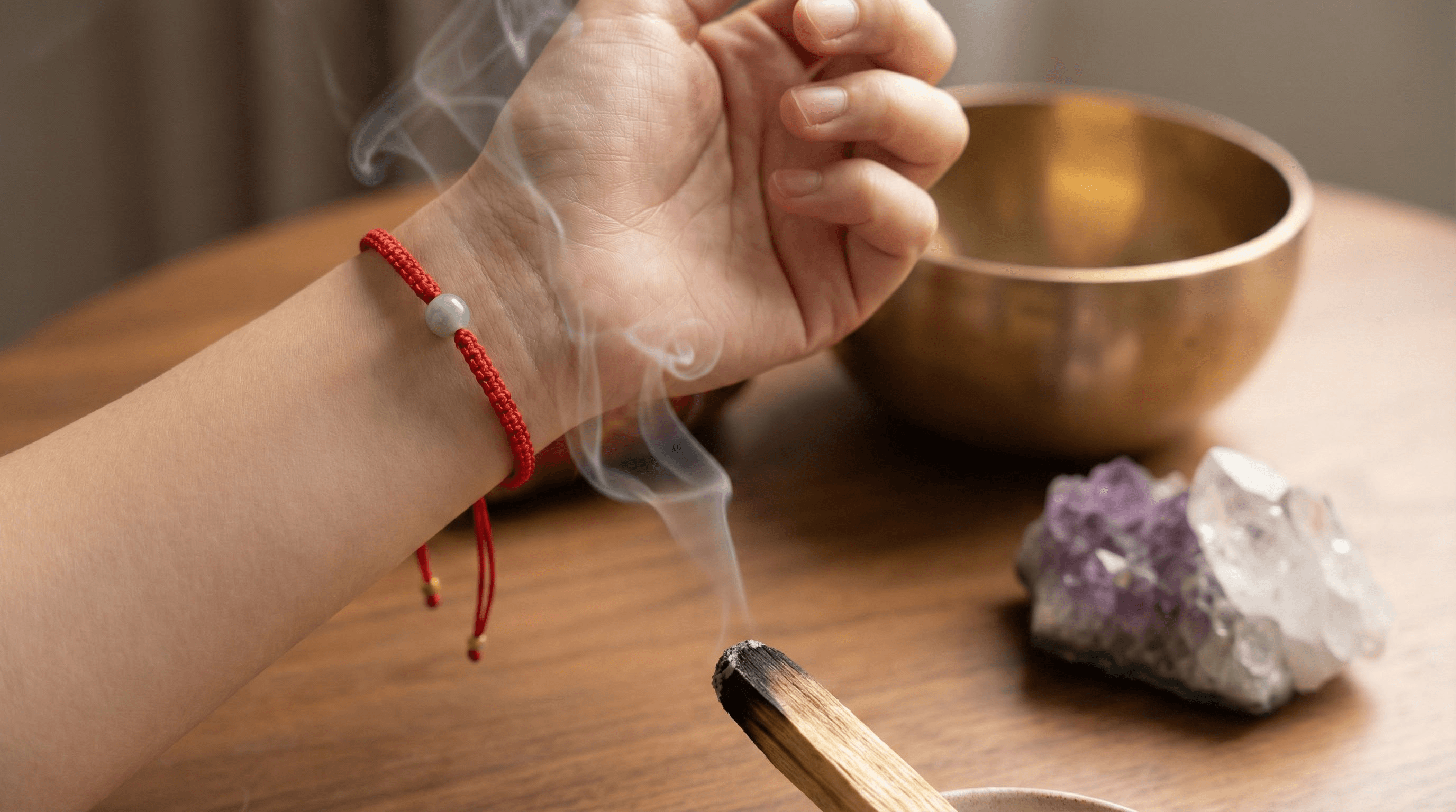 A person cleansing a red string bracelet with incense smoke on their left hand, demonstrating how to prepare a spiritual zodiac gift.