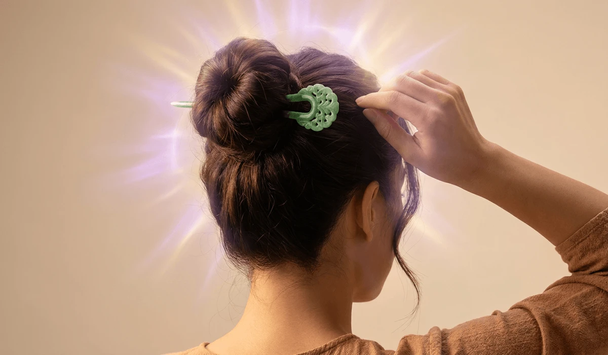 Woman wearing a carved green jade hairpin securing a high bun with subtle glowing Crown Chakra energy aura.