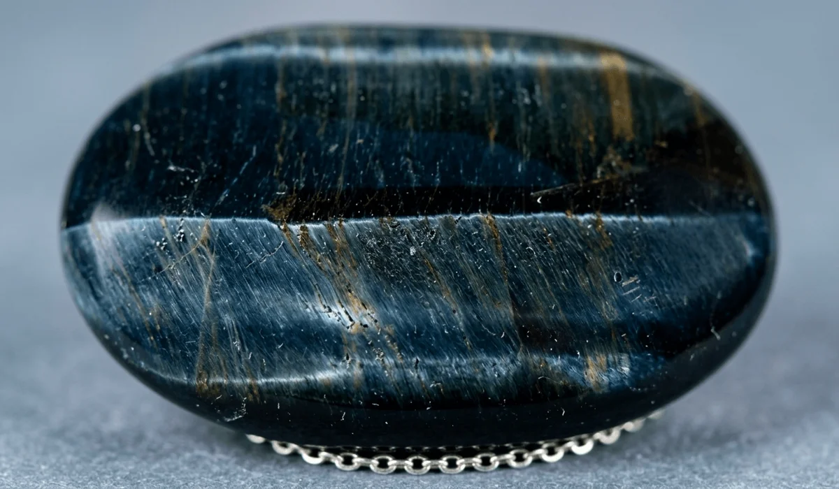 Macro shot of a polished dark blue Hawk's Eye stone showing silky chatoyancy and blue tiger eye luster.