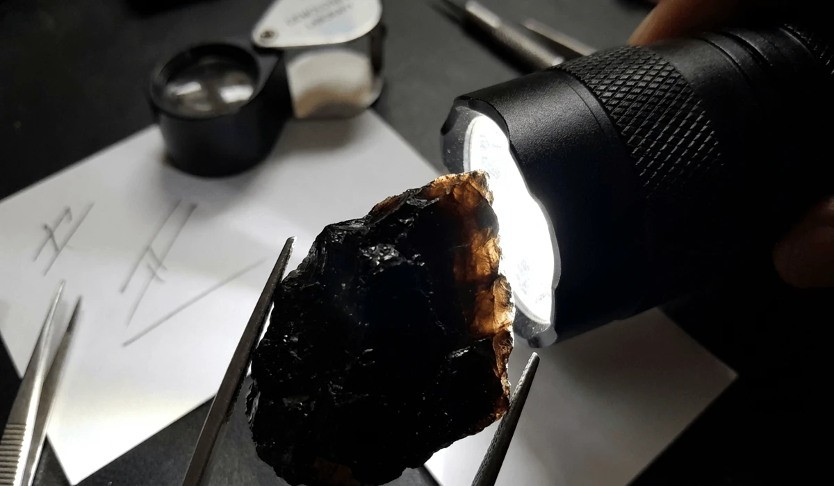 Flashlight authenticity test on real Black Tourmaline revealing a warm brownish tint along the thin edges.