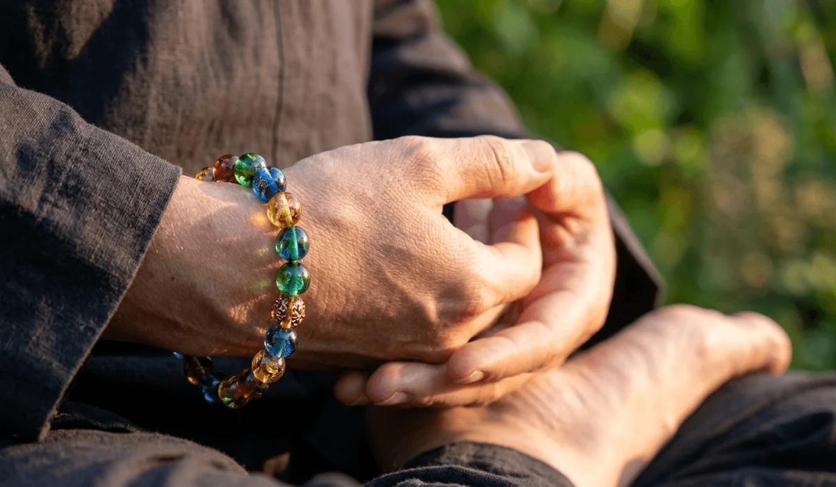 Close-up of a person wearing a multi-colored Liuli crystal bracelet during a mindfulness meditation session.