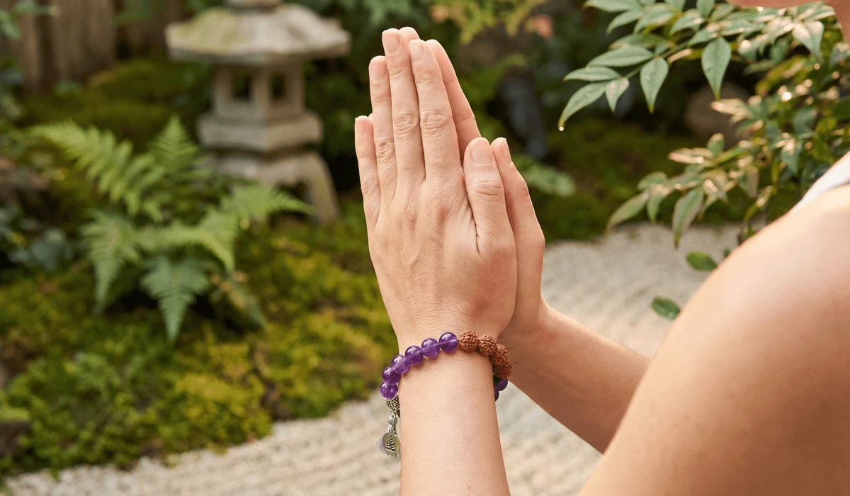 A woman wearing a new amethyst wrist mala in a prayer position, symbolizing the start of a new spiritual journey.