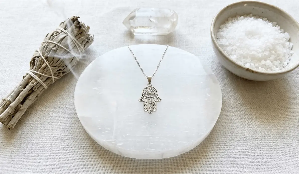 Spiritual cleansing tools including sage, sea salt, and selenite for purifying a Hamsa Hand talisman.