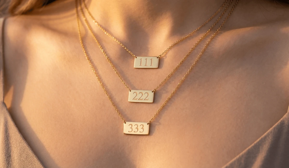 A close-up of tiered gold angel number necklaces featuring 111, 222, and 333 pendants, representing spiritual layering trends.