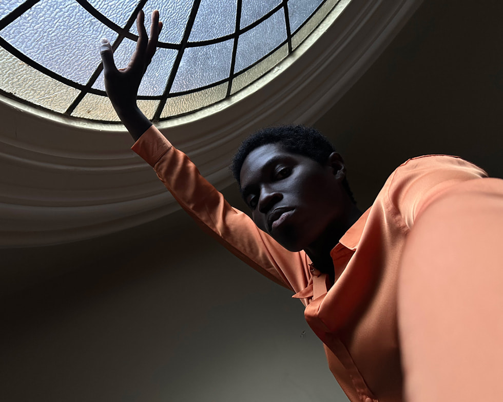 一个穿着橘黄色上衣的人用一只手自拍,另一只手撑着一面玻璃。