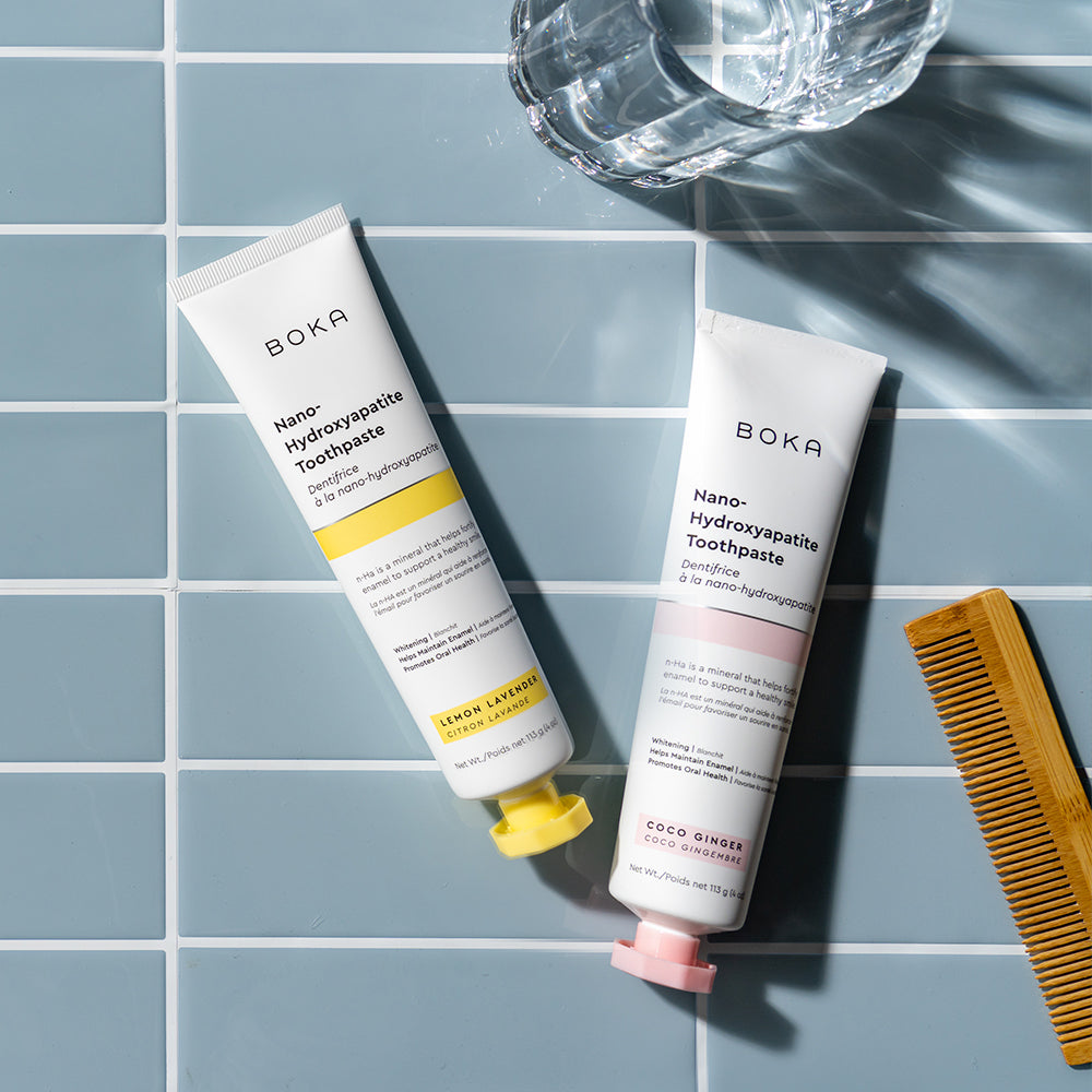 Two n-Ha Toothpaste 2-Pack tubes on blue tiles—fortify enamel, remineralize teeth; glass, comb nearby.