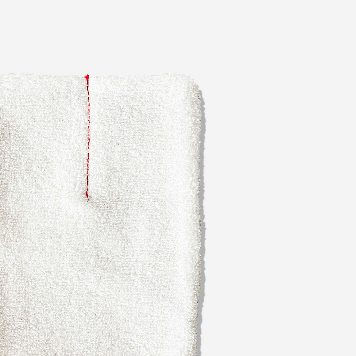 Close-up of top right corner of body scrub mitt. Mitt is terry cotton in cream with red vertical piping.