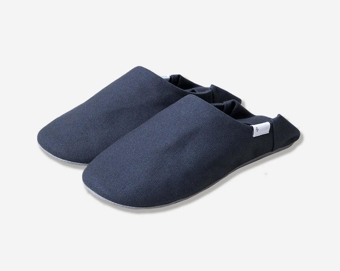 Angled view of navy slippers with heel flap folded down. Shot against a white background. White label with black logo.