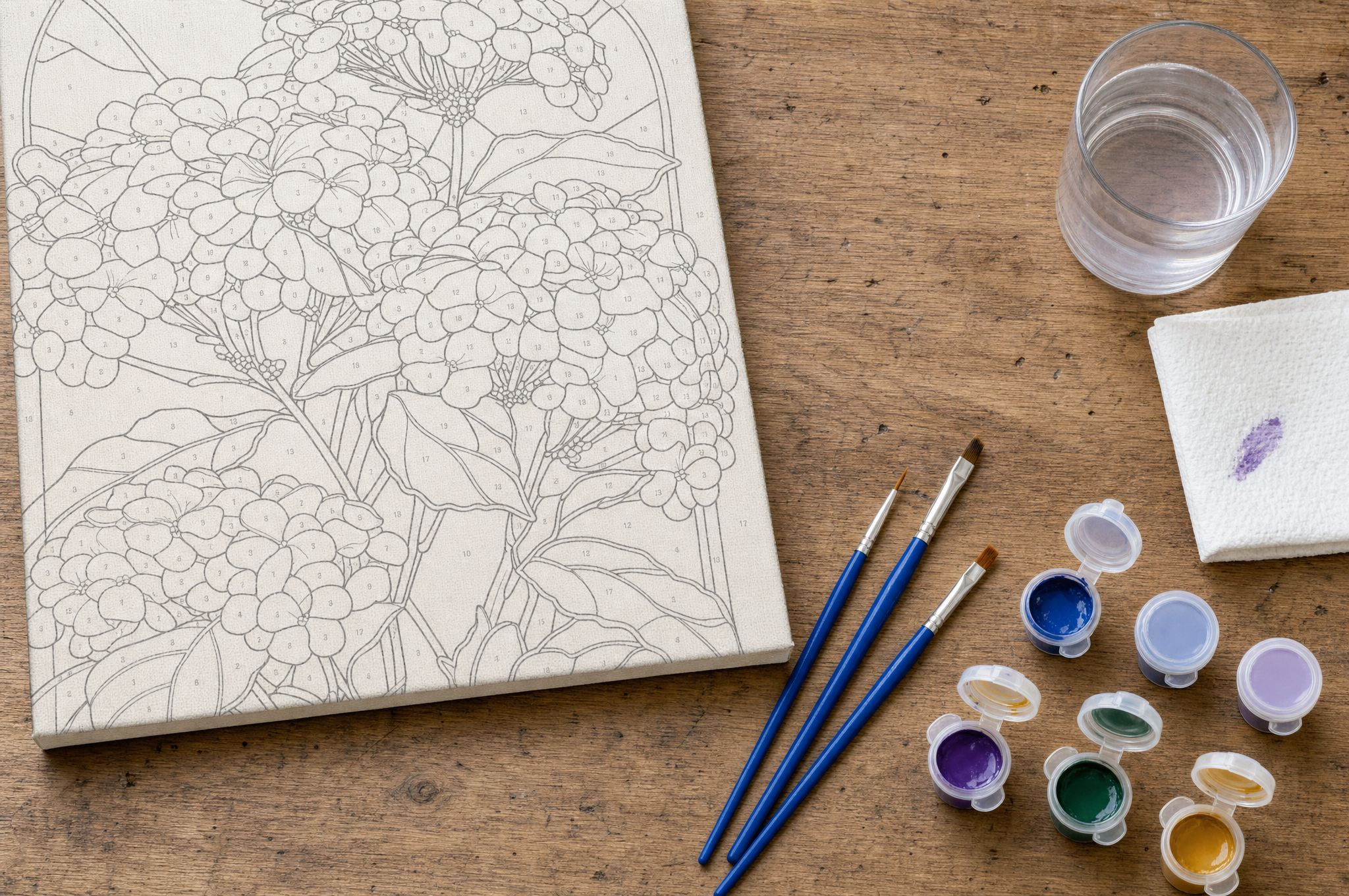 Close-up of paint by numbers supplies: numbered paint pots, brushes and a canvas corner with numbered outline sections