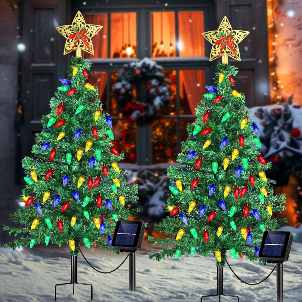 Two solar Christmas tree pathway lights with multicolor C6 LEDs and star toppers staked in snow in front of a decorated home entryway