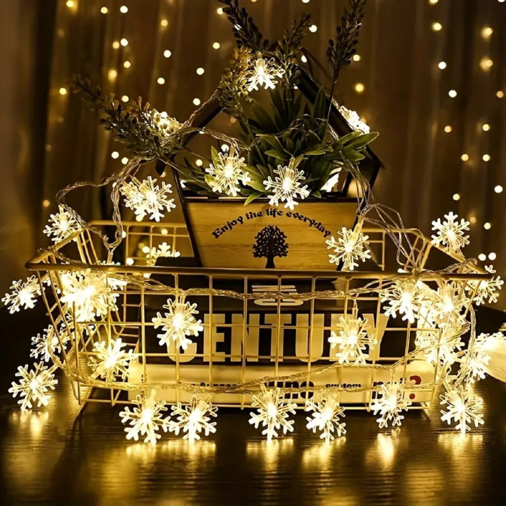 Battery powered LED snowflake curtain lights displayed in warm white glow on a wooden crate with dried botanical decor