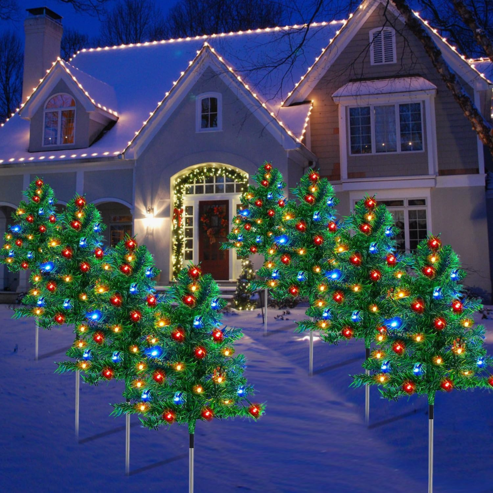 Eight solar Christmas tree pathway lights with multicolor bulbs staked in a snowy yard in front of a holiday-lit house facade