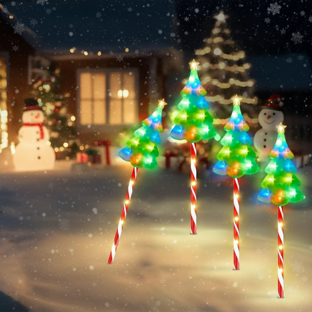 Four solar candy cane Christmas pathway lights with lit tree toppers staked in snowy yard with falling snow