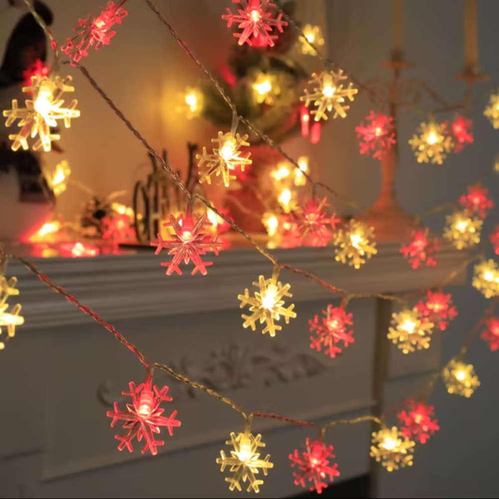 Battery powered snowflake LED string lights in warm red and white tones draped along a mantel shelf
