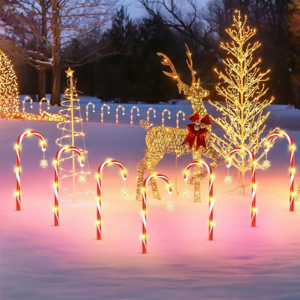 Solar candy cane pathway lights arranged in a yard alongside lit reindeer and spiral tree decorations in a snowy garden scene