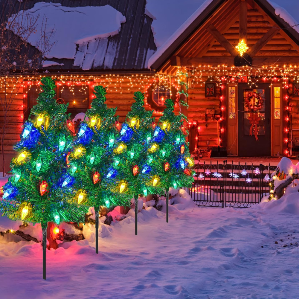 Solar Christmas tree pathway lights with multicolor LED ornaments staked along a snowy walkway toward a decorated house at dusk