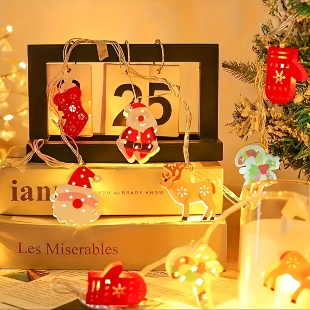 Battery powered Christmas LED string lights with holiday character pendants draped near a wooden calendar and stacked gift boxes in an indoor holiday scene