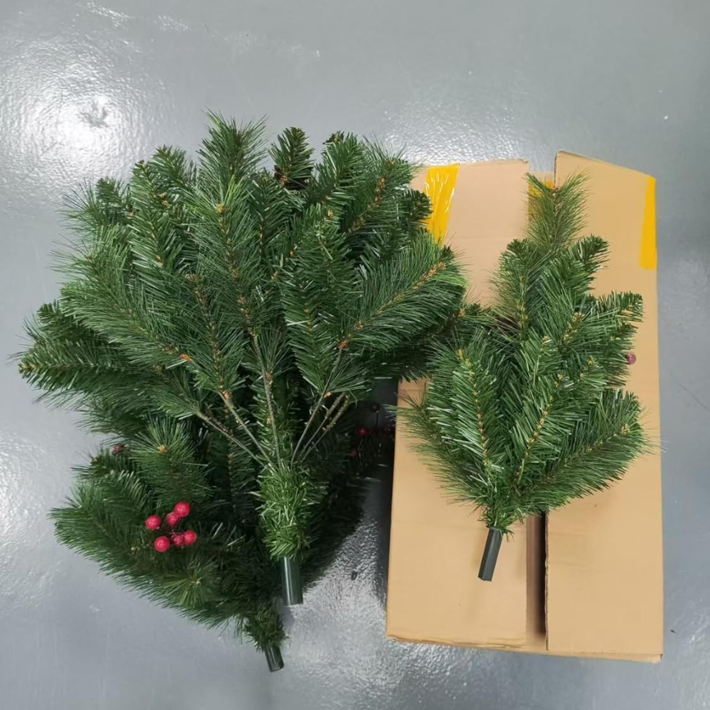 Unboxed solar Christmas tree pathway light components showing green PVC branch bundles and red berry sprigs laid on a gray surface