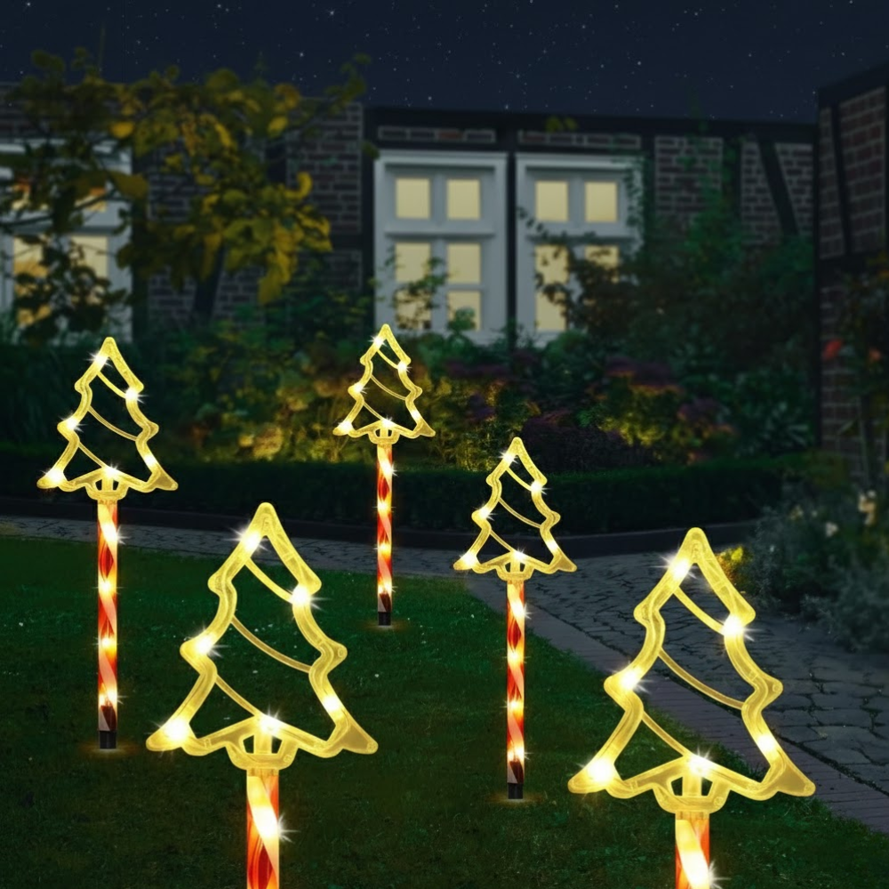 Solar Christmas tree silhouette stake lights on candy cane poles at night, warm white glow against a garden fence and house exterior