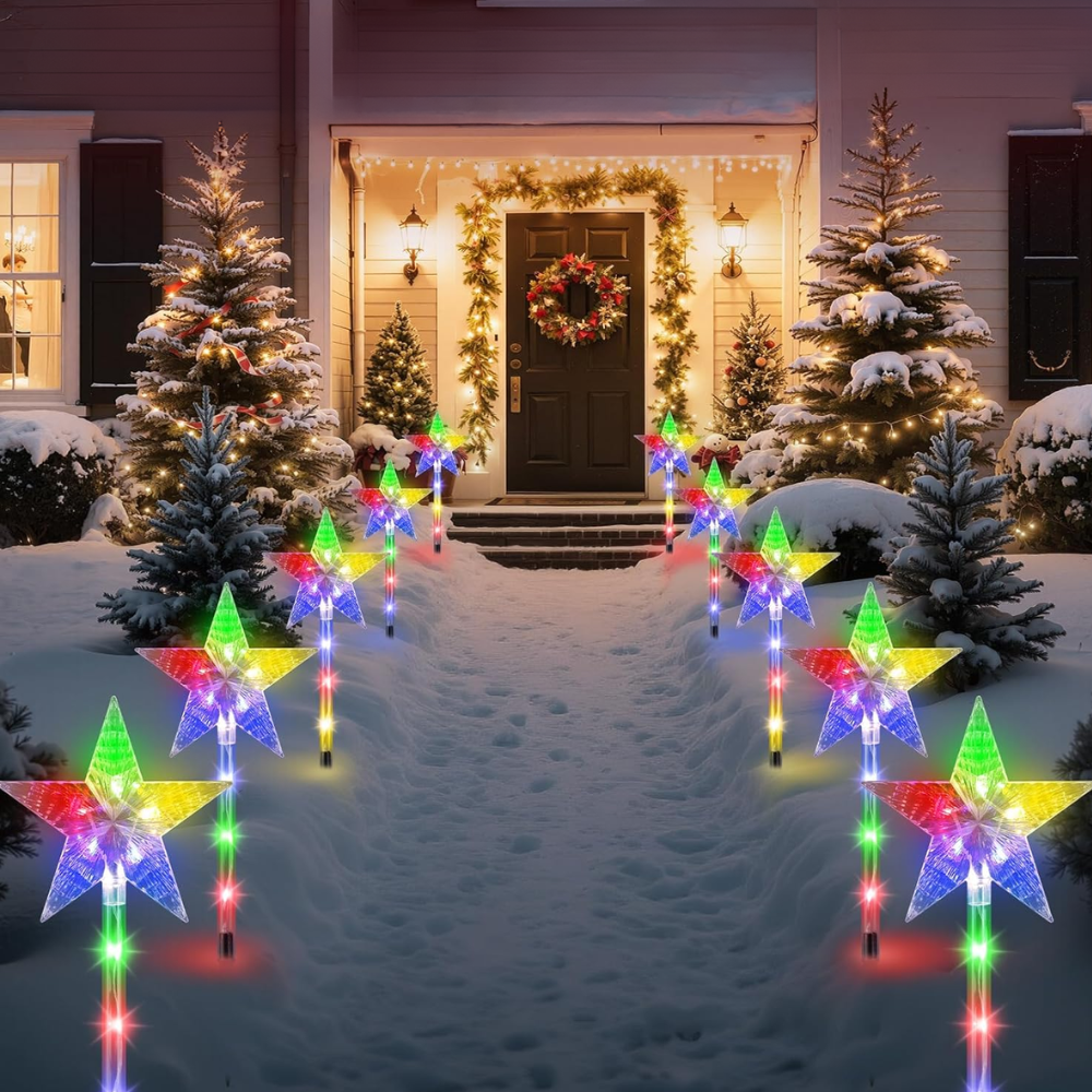 Multicolor star-shaped solar Christmas pathway stake lights glowing along snowy front yard at night