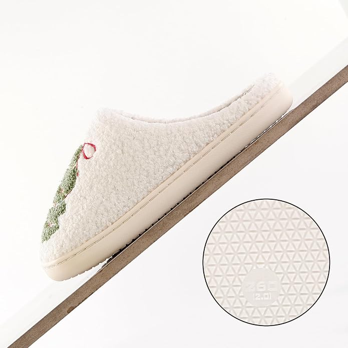 Cream sherpa slipper with a green Christmas tree and red bow embroidery on the toe, shown from the side. A circular inset displays the textured geometric non-slip rubber sole pattern.