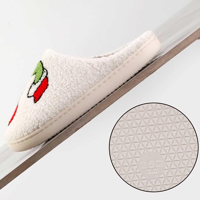 White fluffy slipper with a red and green apple motif on the toe, shown from the side on a diagonal surface. A circular inset shows the textured geometric rubber outsole pattern.
